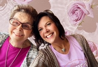 Two women posing for a picture in front of pink flowers.